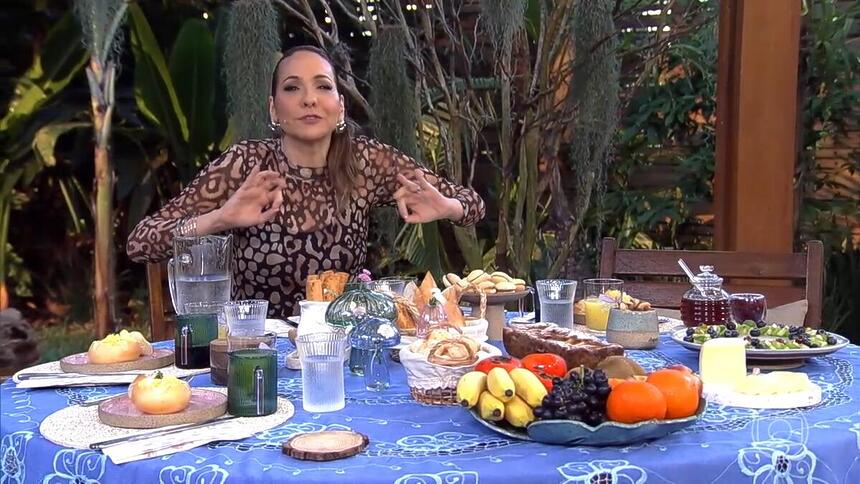 Maria Beltrão abre os braços sentada na mesa do É de Casa