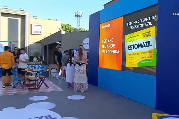 Cenário da atividade patrocinada pelo Estomazil na área externa da Mansão do A Grande Conquista contendo mesinhas, pastel, hambúrguer e muito mais