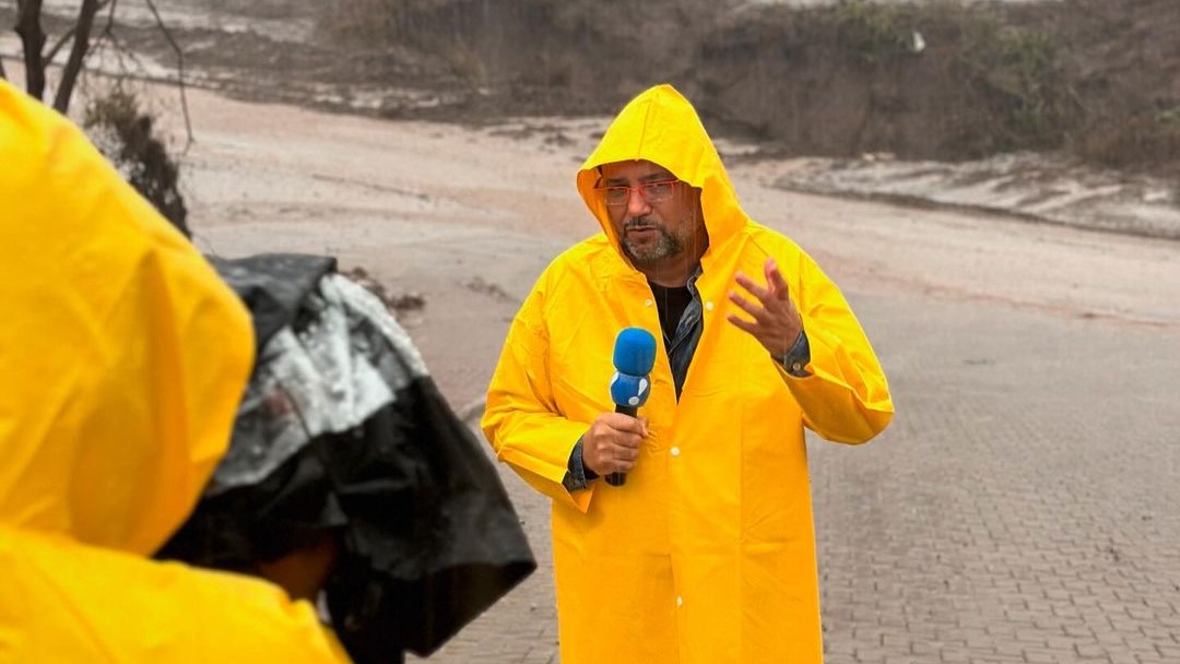 Geraldo Luis segura microfone da RedeTV! com capa de chuva no Rio Grande do Sul