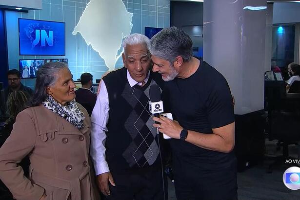 Dona Jurema, seu Luis e William Bonner na redação da RBS TV sorrindo durante o Jornal Nacional