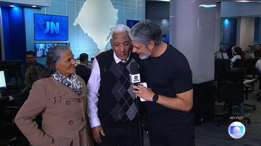 Dona Jurema, seu Luis e William Bonner na redação da RBS TV sorrindo durante o Jornal Nacional