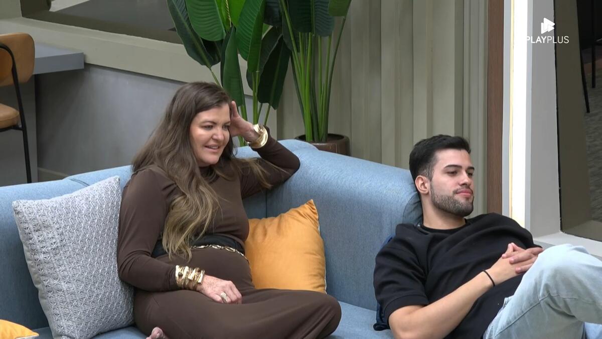 Dona Geni com a mão na cabeça no sofá do A Grande Conquista 2