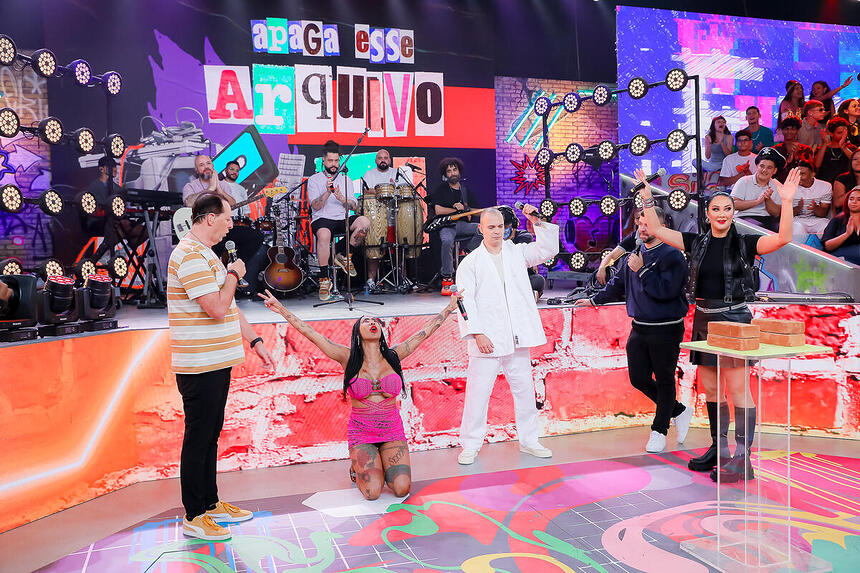 Inês Brasil ajoelhada no centro do palco do É Tudo Nosso com os braços para cima agradecendo