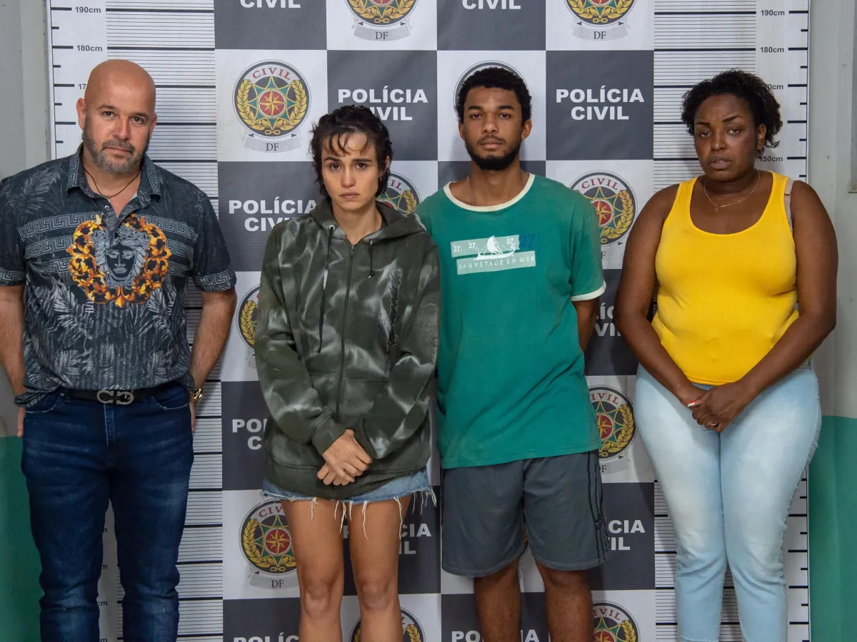 Imagem mostra o elenco principal com as mãos algemadas em frente ao painel da Polícia Civil.