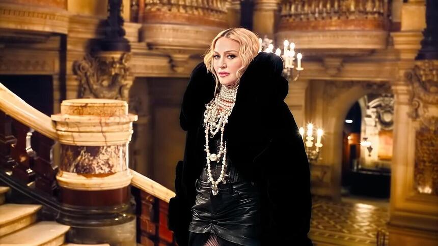 Madonna subindo escadas, de casaco preto, em comercial do banco Itaú. Cantora não ajudou o Rio grande do Sul