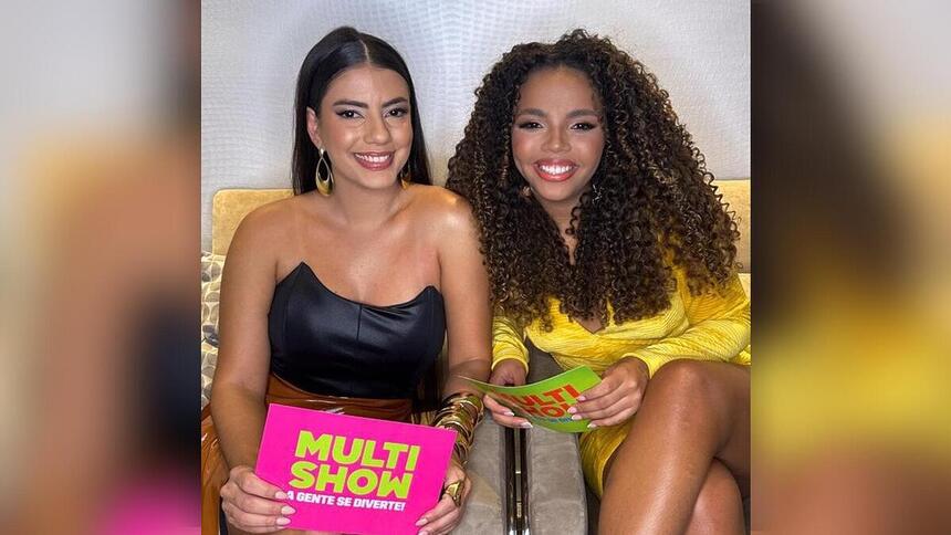 Fernanda e Pitel seguram fichas do Multishow nos bastidores do canal. As duas estão sorrindo