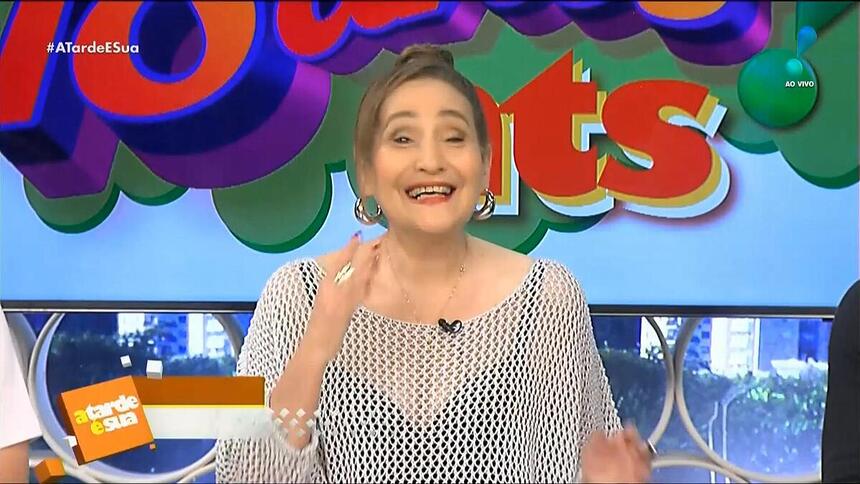 Sonia Abrão sorrindo em frente ao logo do A Tarde é Sua 18 anos