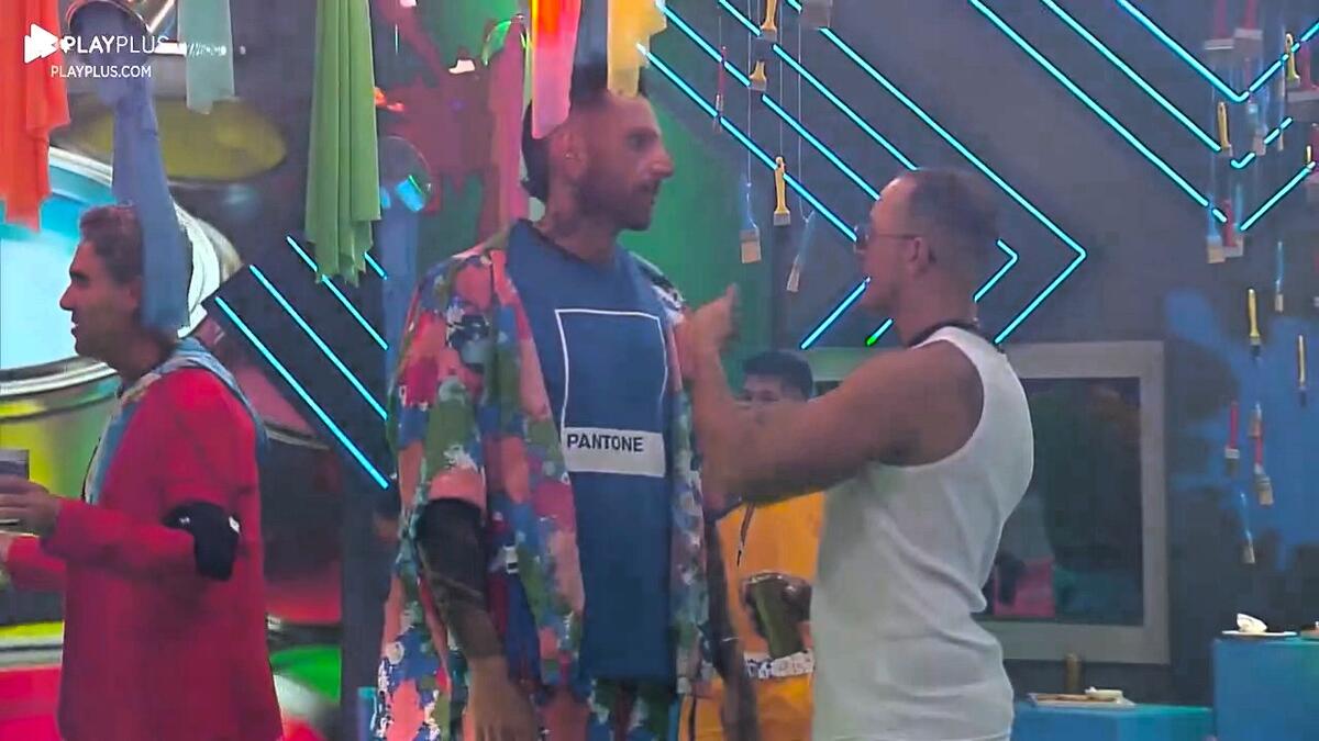 Guipa olha para Fellipe no centro do palco da Festa das Cores, eles falam de Dona Geni no A Grande Conquista