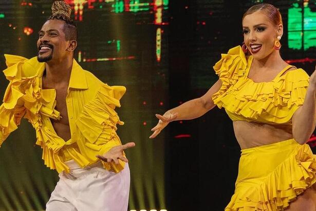 Samuel de Assis e Larissa Parison, com roupa amarela, dançando salsa na Dança dos Famosos