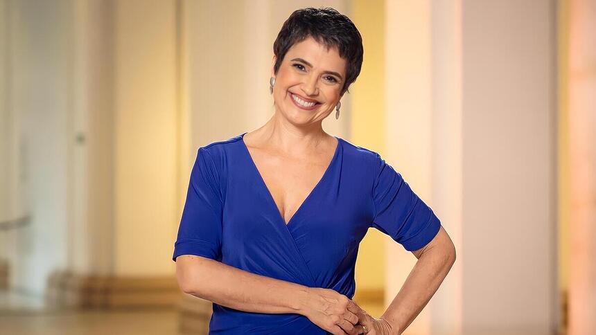 Sandra Annenberg de vestido azul, sorrindo, em gravação da Globo