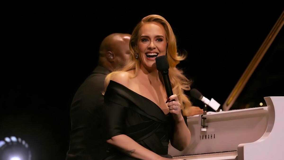 Adele sorrindo em apresentação ao lado de pianista