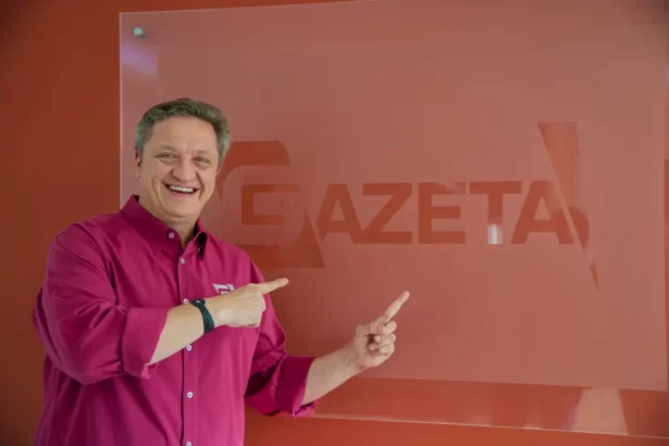 Alex Müller aponta para o logo da TV Gazeta sorrindo