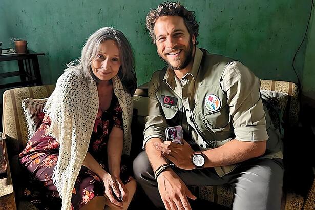 Débora Duarte sorrindo ao lado do ator Elam Lima nos bastidores das gravações de A Caverna Encantada