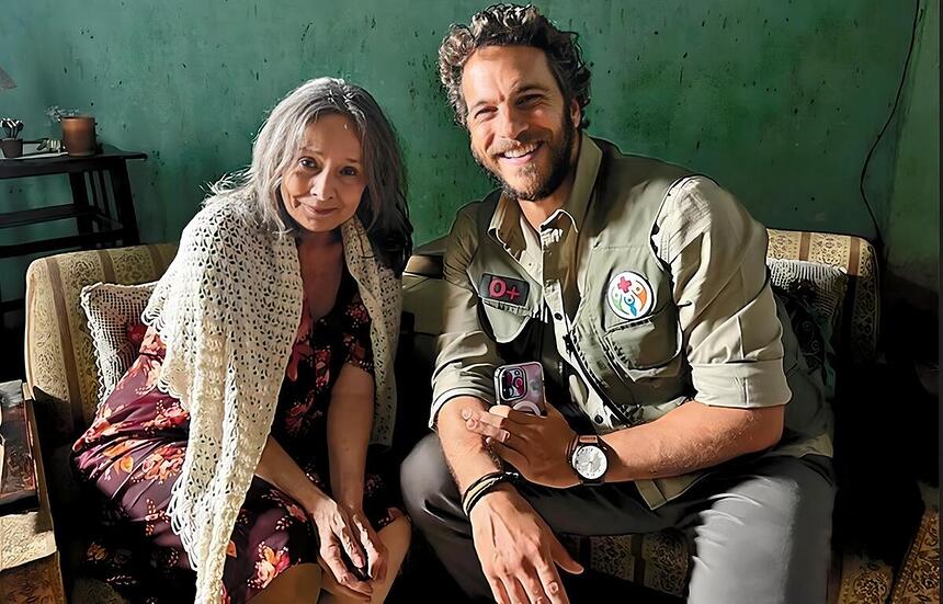 Débora Duarte sorrindo ao lado do ator Elam Lima nos bastidores das gravações de A Caverna Encantada