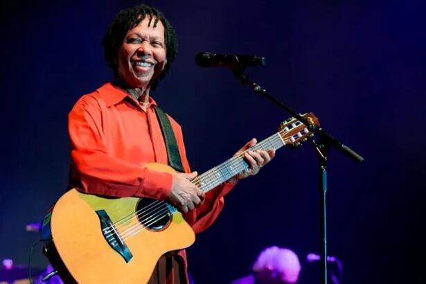 Djavan sorrindo e tocando violão em show