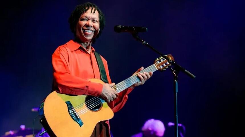 Djavan sorrindo e tocando violão em show