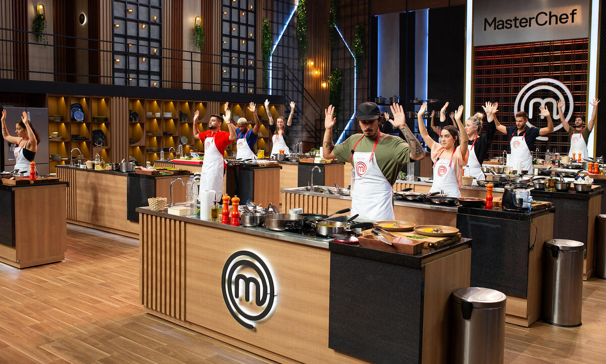 12 primeiros participantes do MasterChef Brasil levantam as mãos indicando que terminaram a prova