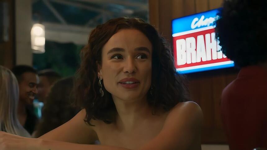 Kika sorrindo em um bar, conversando com Eriberto em cena da novela Renascer