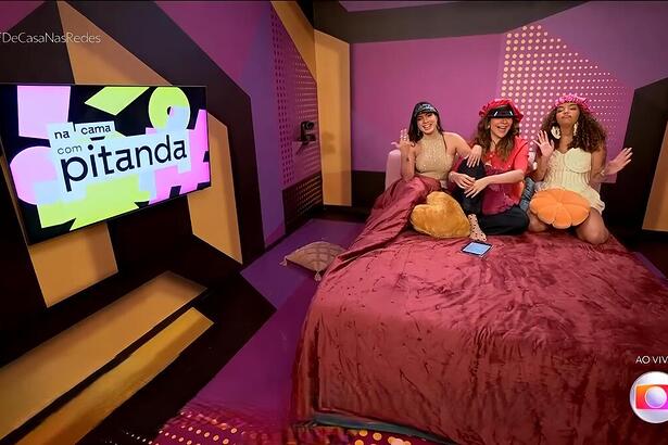 Fernanda e Pitel sentados ao lado de Maria Beltrão na cama do programa Na Cama com Pitanda