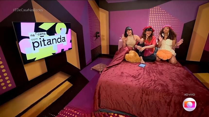 Fernanda e Pitel sentados ao lado de Maria Beltrão na cama do programa Na Cama com Pitanda