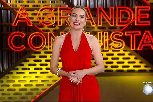 Rachel Sheherazade de vermelho sorrindo no cenário do A Grande Conquista 2