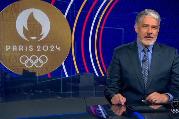 Bonner durante o bloco olímpico do Jornal Nacional, com o logo de Paris 2024 ao fundo da redação