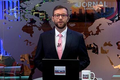 Cassius Zeilmann sorrindo na estreia do novo cenário da BandNewsTV ele está posicionado em frente a redação