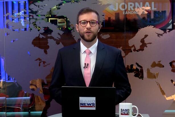 Cassius Zeilmann sorrindo na estreia do novo cenário da BandNewsTV ele está posicionado em frente a redação