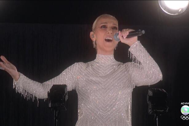 Céline Dion com os braços abertos cantando na Torre Eiffel na abertura da Olimpíada de Paris 2024