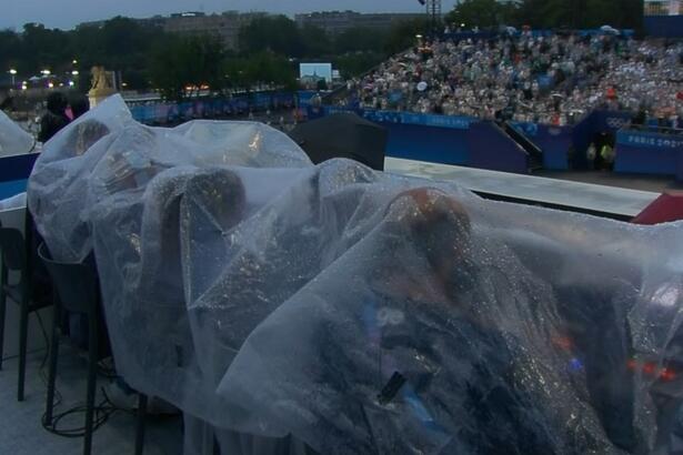 Equipe da Globo sentados debaixo de uma lona que protege da chuva na abertura da Olimpíada de Paris