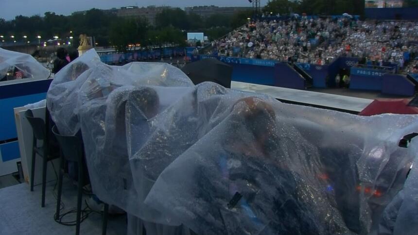 Equipe da Globo sentados debaixo de uma lona que protege da chuva na abertura da Olimpíada de Paris