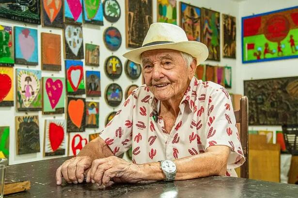 Xilogravurista pernambucano J. Borges sentado em uma mesa com chapéu branco na cabeça