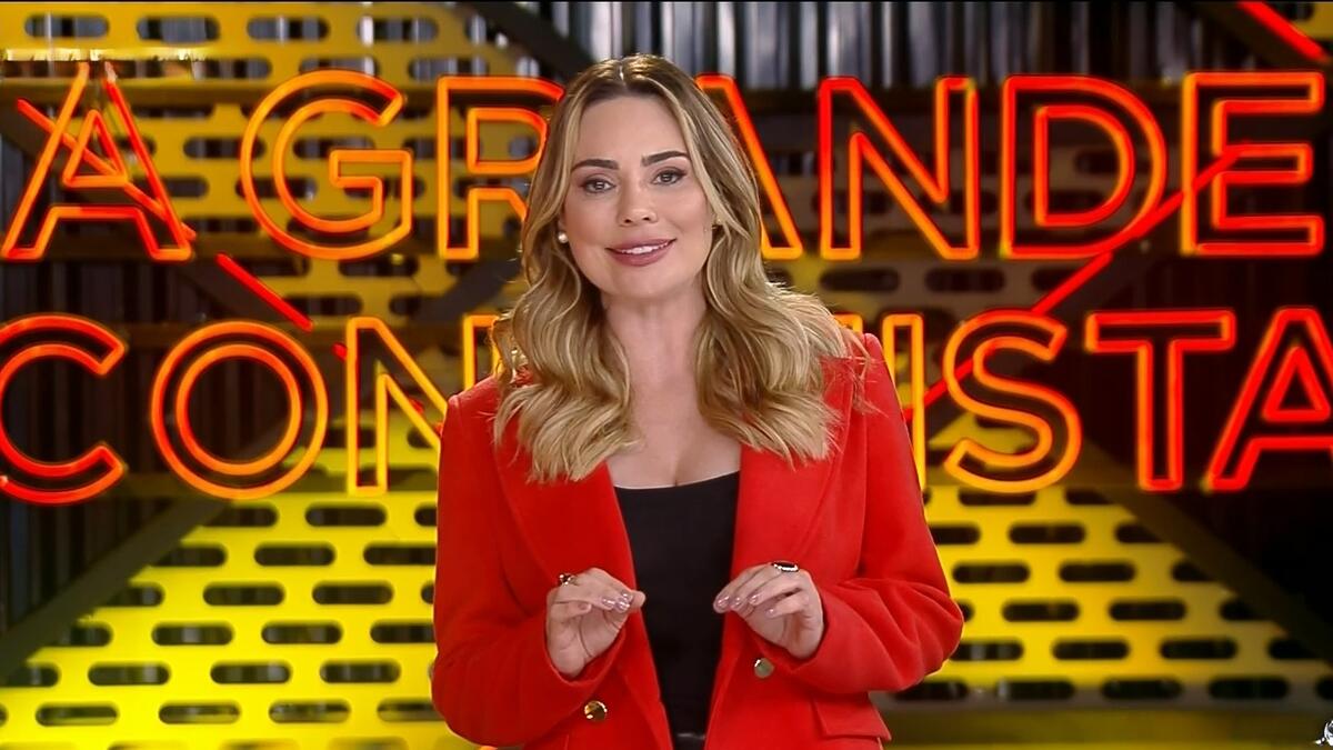 Rachel Sheherazade veste um casaco vermelho e sorrir enquanto apresenta o A Grande Conquista 2