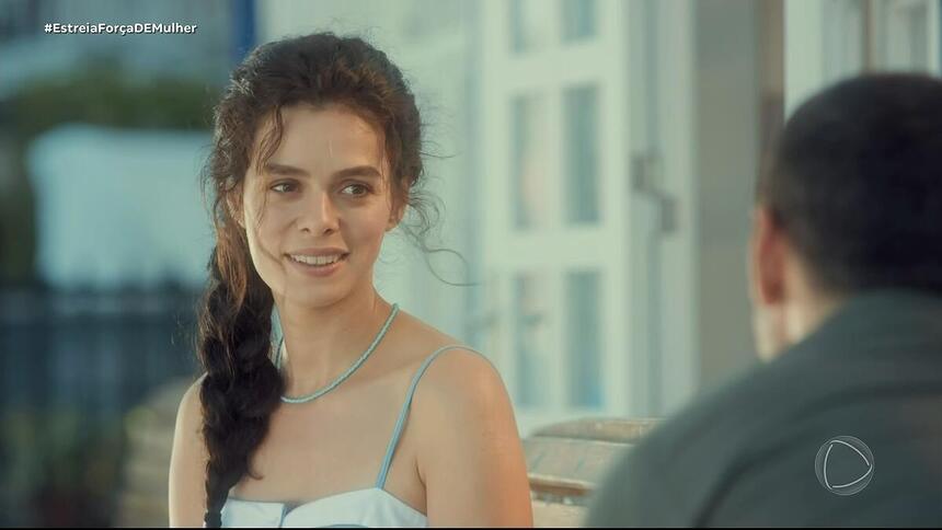 Özge Özpirinçci, protagonista da novela turca Força de Mulher, olha para um homem e sorrir, sentados em um banco de praça