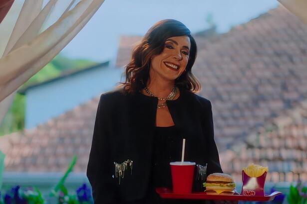 Christiante Torloni sorrindo em nova campanha da Bob's. Ela segura uma bandeja com hamburguer e Coca-Cola