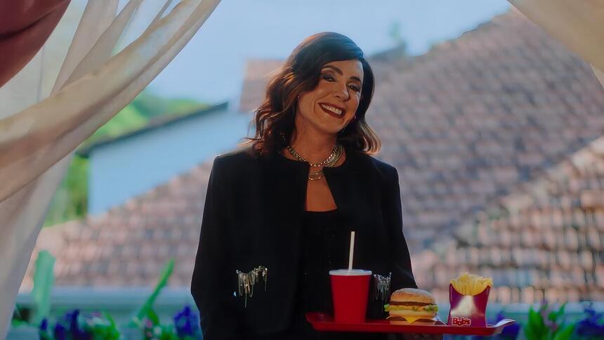 Christiante Torloni sorrindo em nova campanha da Bob's. Ela segura uma bandeja com hamburguer e Coca-Cola