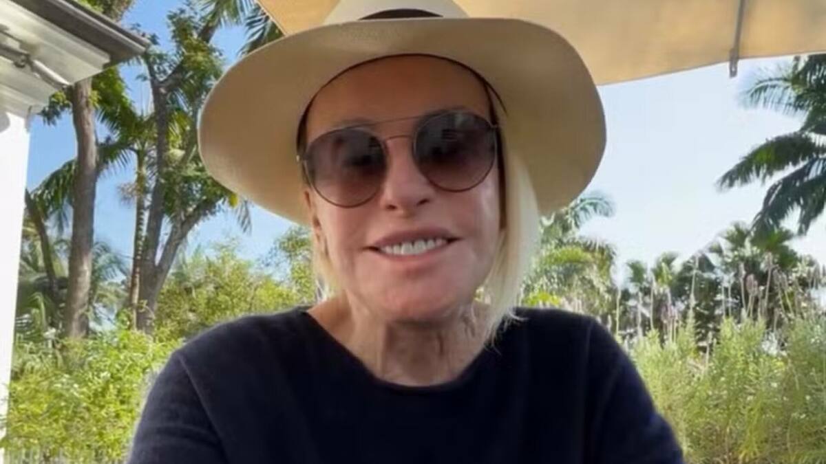 Ana Maria Braga com um sorriso no rosto, com óculos e chapéu de sol
