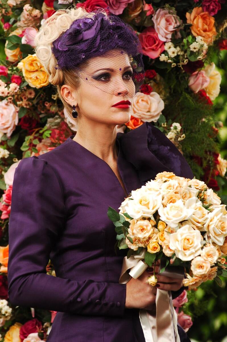 Cristina de vestido roxo segura o buquê de flores