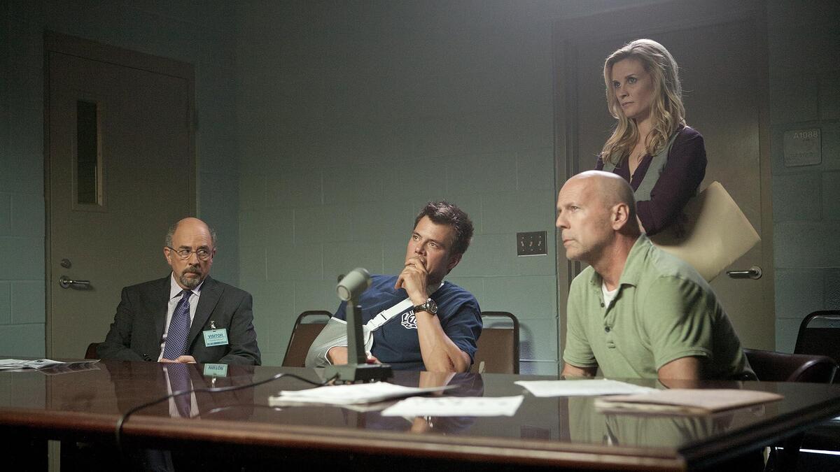 Bruce Willis sentado ao lado de policiais em cena do filme Fogo contra Fogo