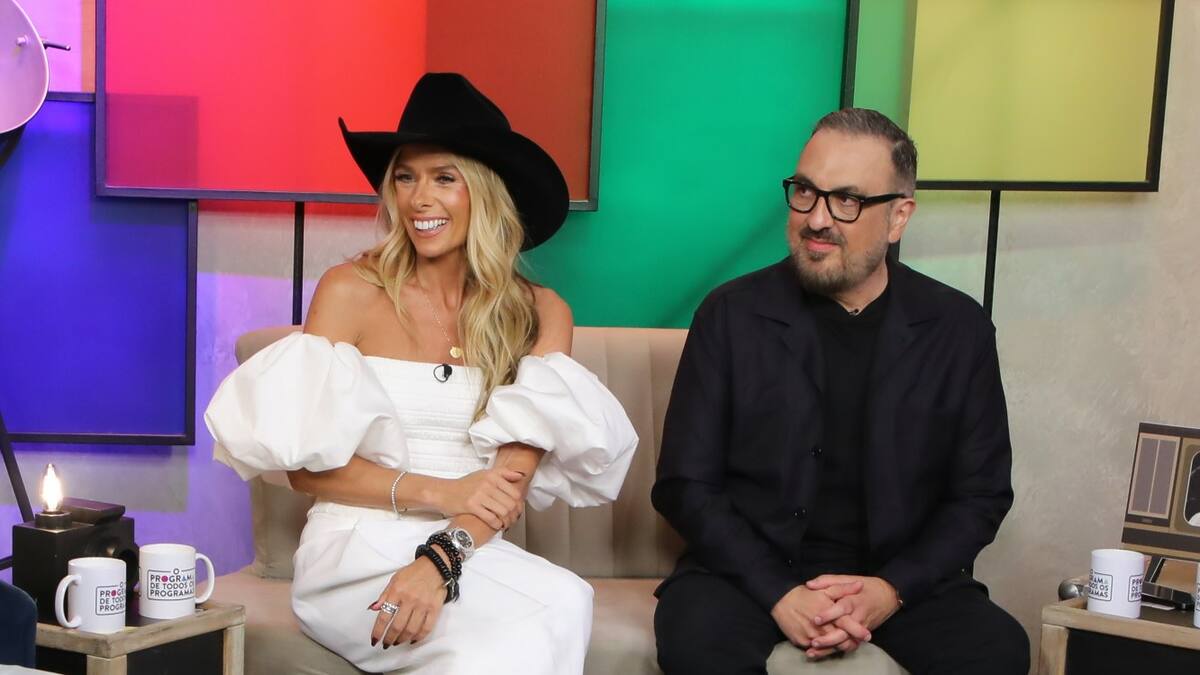 Adriane Galisteu e Rodrigo Carelli sorridentes e sentados no sofá do Programa de Todos os Programas no Portal R7