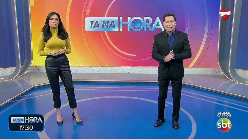 Marcia Dantas em pé ao lado de Marcão do Povo no centro do cenário do Tá na Hora no SBT