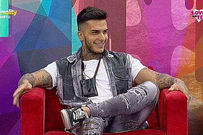 Nuno da Silva sentado em um sofá e sorrindo em gravação do reality show Love On Top