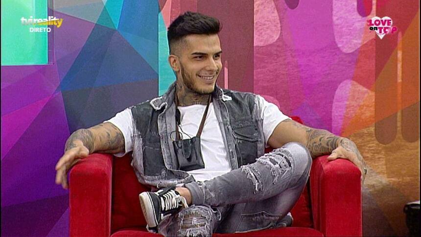 Nuno da Silva sentado em um sofá e sorrindo em gravação do reality show Love On Top