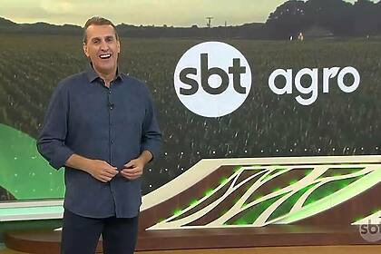 Apresentador Sandro Ivanowski no cenário do SBT Agro, em frente ao telão e sorrindo