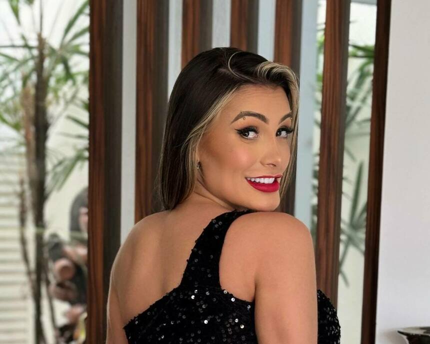 Andressa Urach de top preto, batom vermelho e olhando de lado