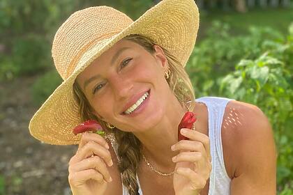 Gisele Bündchen segura duas frutas nas mãos e sorrir com chapéu de camponesa