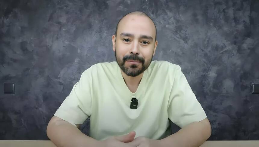 Klenion Livio de camisa bege sentado com semblante triste, em sua bancada, gravando para o YouTube