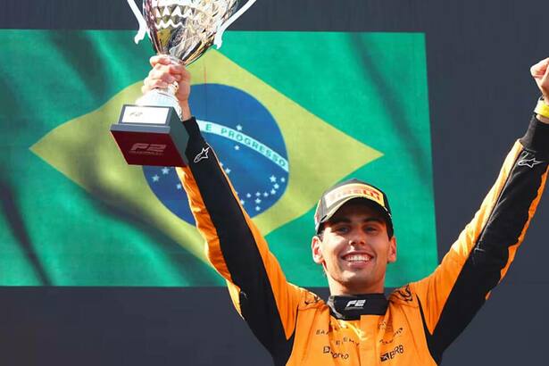 Gabriel Bortoleto com um troféu em mãos e uma bandeira do Brasil ao fundo