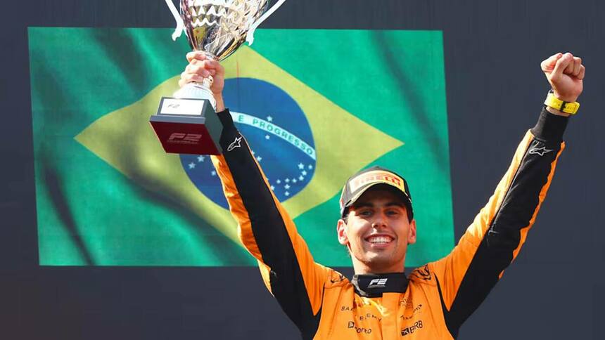 Gabriel Bortoleto com um troféu em mãos e uma bandeira do Brasil ao fundo