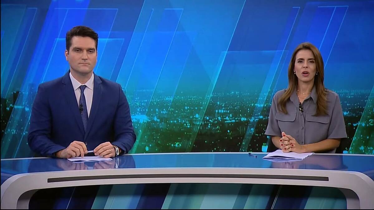 Apresentadores do JRNews posicionados na bancada do telejornal